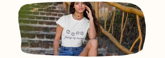 Femme portant un t-shirt streetwear « flexing my mussels » avec moules, assise sur escalier en extérieur, style décontracté rose zombie.